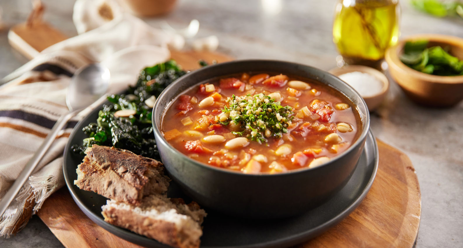 A bowl of minestrone soup with bread and a salad