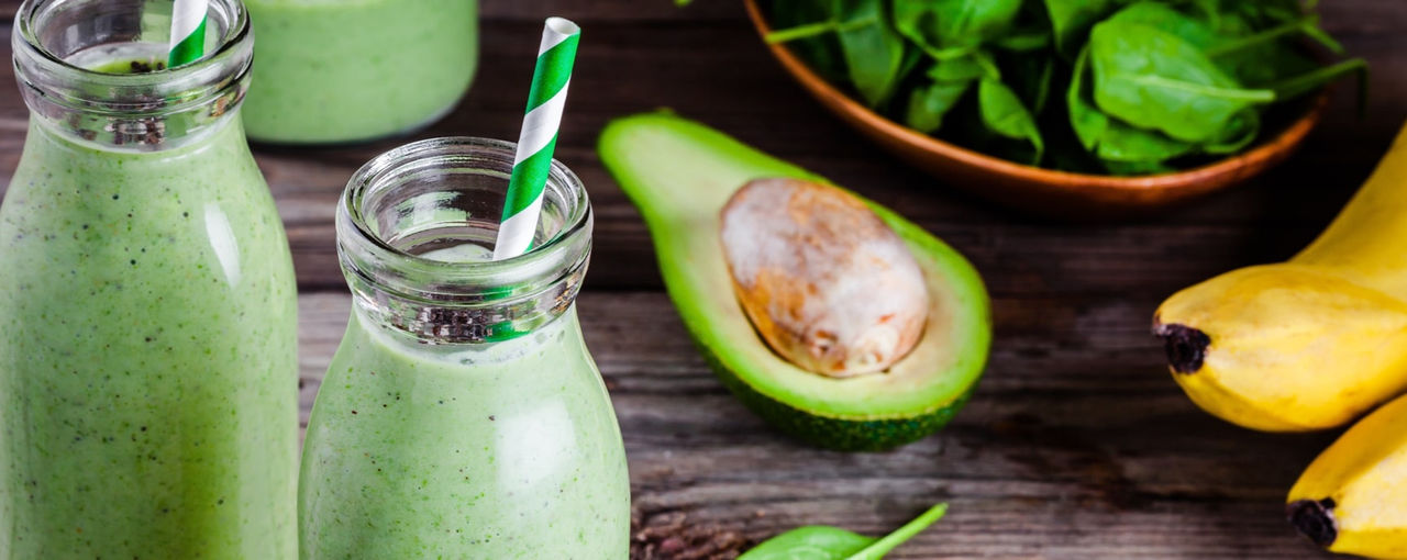 Green smoothies next to an avocado Green smoothies next to an avocado